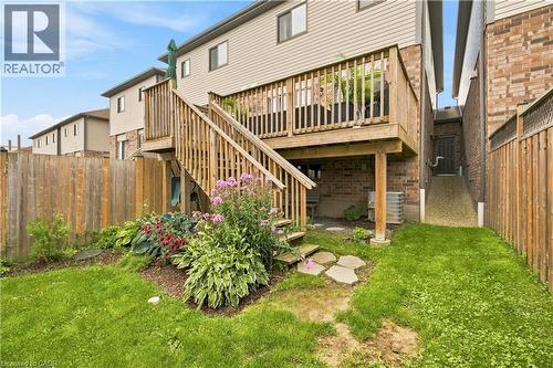 Expansive wood deck with stairs, brick and siding exterior, established garden beds, grassy lawn, and wood fencing - 187 Eden Oak Trail, Kitchener, ON 