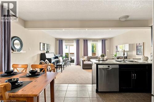 Open-concept living space with tile flooring, a kitchen island with a double basin sink and stainless steel dishwasher, and a dining area with wood-finish table and chairs - 187 Eden Oak Trail, Kitchener, ON 