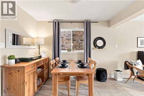 Warm wood cabinetry and dining table anchor this open dining area, featuring tile flooring, recessed ceiling lighting, and French doors framed by floor-to-ceiling windows with blackout curtains - 187 Eden Oak Trail, Kitchener, ON 