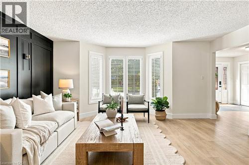 Living area featuring a dark accent panel wall, light wood-finish flooring, and bay windows with plantation shutters - 62 Corfield Drive, Kitchener, ON 