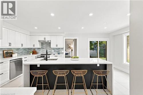 Modern kitchen featuring white shaker cabinetry, stainless steel appliances, a light blue tile backsplash, and a large island with a white countertop - 62 Corfield Drive, Kitchener, ON 