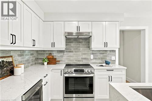 White shaker-style cabinetry with matte black hardware, light-toned countertops, full-height gray subway tile backsplash, and stainless steel appliances - 62 Corfield Drive, Kitchener, ON 