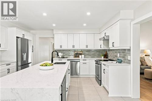 Kitchen featuring white shaker cabinetry, stainless steel appliances, a large center island with a black faucet, and a subway tile backsplash - 62 Corfield Drive, Kitchener, ON 