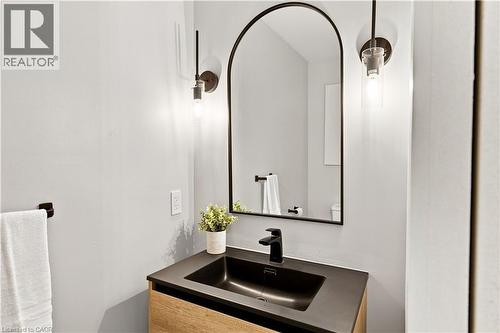 Arched mirror with black frame, wood-finish vanity, matte black faucet, dark basin, and wall-mounted light fixtures - 62 Corfield Drive, Kitchener, ON 
