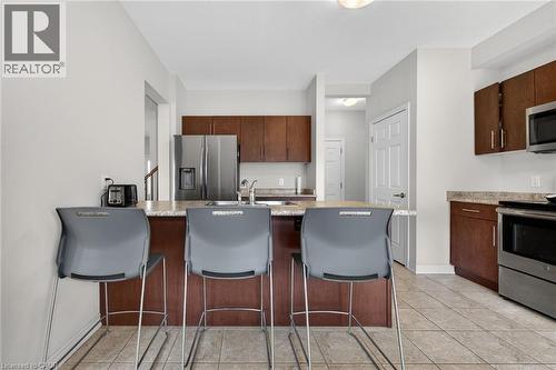 Kitchen featuring a breakfast bar, stainless steel appliances, wood-finish cabinetry, and tiled flooring - 9 Winterberry Boulevard, Thorold, ON 