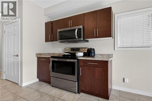 Stainless steel range and microwave, wood-finish cabinetry, light-toned countertop, and tiled flooring - 9 Winterberry Boulevard, Thorold, ON 