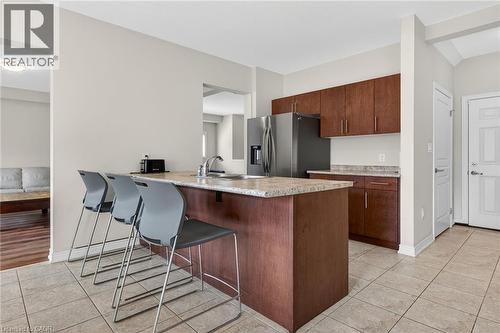Kitchen featuring wood-finish cabinetry, stainless steel refrigerator, and a breakfast bar with stone-finish countertop - 9 Winterberry Boulevard, Thorold, ON 