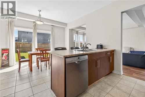 Kitchenette with wood-finish cabinetry, light-toned countertop, stainless steel dishwasher, and tiled flooring - 9 Winterberry Boulevard, Thorold, ON 