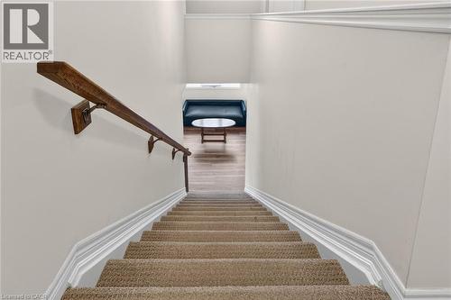 Carpeted stairs with a wood handrail, white trim, and light wall finishes - 9 Winterberry Boulevard, Thorold, ON 