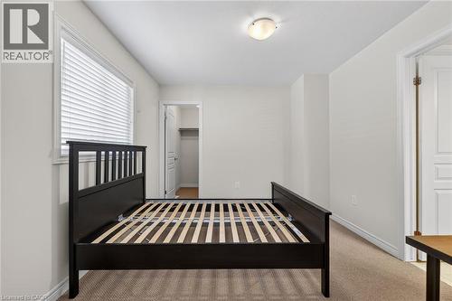 Carpeted bedroom featuring a large window with blinds, ceiling-mounted light fixture, and a built-in closet with shelving - 9 Winterberry Boulevard, Thorold, ON 