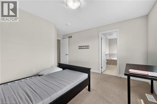 Neutral wall paint, carpet flooring, ceiling-mounted light fixture, white interior doors, and a partial view of a tiled bathroom with a built-in tub - 9 Winterberry Boulevard, Thorold, ON 