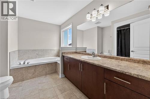 Built-in bathtub with tiled surround, large vanity with integrated sink, expansive mirror, and overhead lighting - 9 Winterberry Boulevard, Thorold, ON 