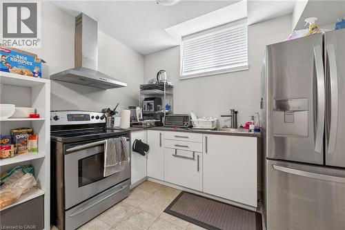 Stainless steel range with coordinating range hood, stainless steel refrigerator, white cabinetry, dark countertops, and tile flooring - 9 Winterberry Boulevard, Thorold, ON 
