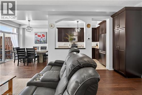 Wood-finish flooring throughout, with a dining area featuring a modern chandelier, and a kitchen with dark cabinetry and stainless-steel appliances - 88 Highgate Drive, Hamilton, ON 
