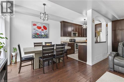 Wood-finish flooring throughout, dining area with a contemporary chandelier, open-concept kitchen with stainless steel appliances, dark wood cabinetry, and a light-toned backsplash - 88 Highgate Drive, Hamilton, ON 