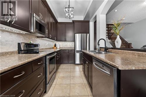 Kitchen featuring rich dark cabinetry, stainless steel appliances, tile flooring, and a mosaic tile backsplash - 88 Highgate Drive, Hamilton, ON 