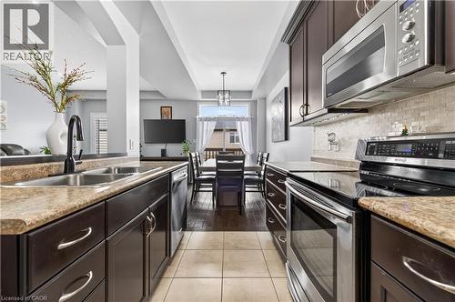 Kitchen featuring dark wood-finish cabinetry, stainless steel appliances, tiled flooring, and a subway tile backsplash - 88 Highgate Drive, Hamilton, ON 