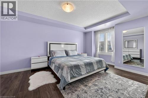 Tray ceiling, recessed lighting, wood-finish flooring, window with white plantation shutters, and a modern white headboard - 88 Highgate Drive, Hamilton, ON 