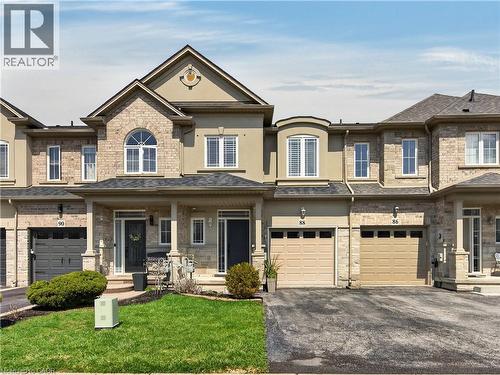 Two-story townhome featuring a stone and stucco exterior, arched windows, covered front entrance, and an attached single-car garage - 88 Highgate Drive, Hamilton, ON 