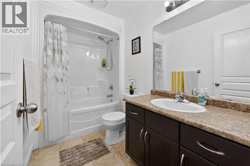 Bathtub with integrated shower, vanity with an undermount sink, dark wood-finish cabinetry, stone-look countertop, and tiled flooring - 88 Highgate Drive, Hamilton, ON 