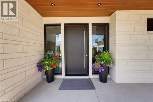 Welcoming entry featuring a dark-finish front door with sidelights, flanked by black planter vessels with seasonal flowers - 5709 Forth Line, Hillsburg, ON 