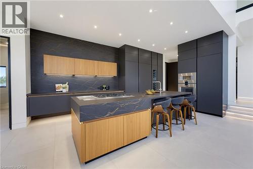 Contemporary kitchen featuring custom cabinetry in deep navy with natural wood-finish island, waterfall-edge countertop with dark stone finish, integrated stainless steel appliances, recessed ceiling - 5709 Forth Line, Hillsburg, ON 
