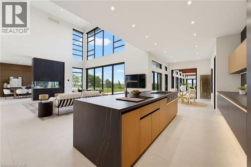 Open-concept kitchen and living area featuring a two-tier island with wood-finish cabinetry and dark countertops, stainless steel appliances, polished concrete flooring, soaring ceilings with skylight - 5709 Forth Line, Hillsburg, ON 