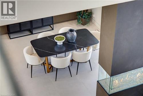 Modern dining area featuring a black wood-finish table with geometric base, four cream upholstered chairs with metal legs, light wood-finish flooring, and a bright, open layout accented by a built-in - 5709 Forth Line, Hillsburg, ON 