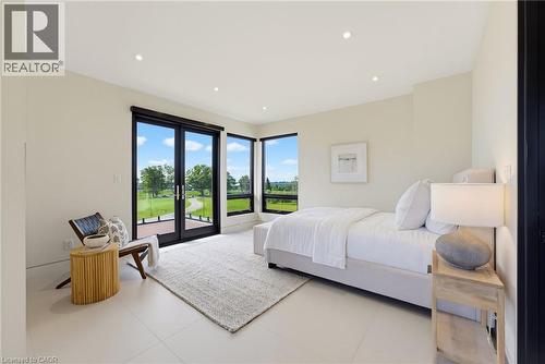 Bright, light-filled primary bedroom featuring floor-to-ceiling glass doors opening to manicured grounds, recessed ceiling lighting, neutral wall finishes, and polished concrete flooring throughout - 5709 Forth Line, Hillsburg, ON 