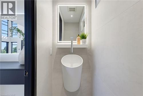 Modern powder room featuring a cylindrical vessel sink with polished chrome wall-mounted faucet, illuminated medicine cabinet with integrated LED mirror, neutral tile flooring, and clean minimalist de - 5709 Forth Line, Hillsburg, ON 