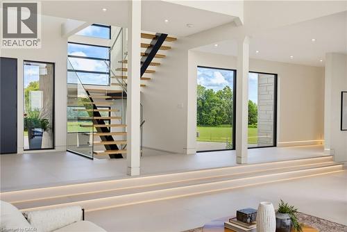 Open-concept living space featuring soaring ceilings with skylights, modern floating staircase with metal railings and wood treads, polished concrete flooring, and expansive glass sliding doors openin - 5709 Forth Line, Hillsburg, ON 