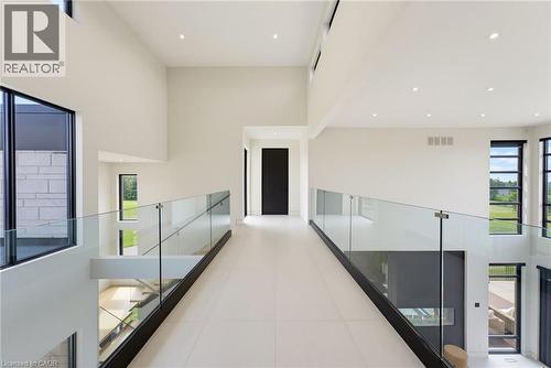Modern hallway featuring polished concrete flooring, floor-to-ceiling white walls with recessed lighting, and glass railings with metal handrails flanking both sides - 5709 Forth Line, Hillsburg, ON 