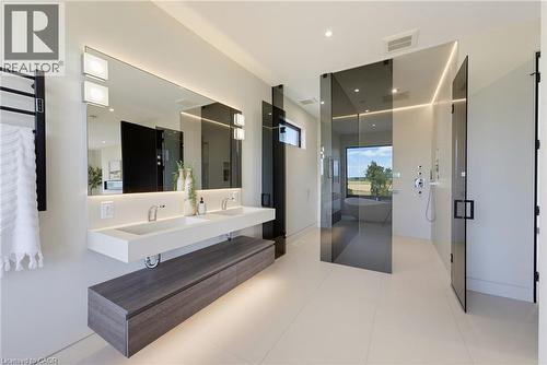 Dual floating vanity with integrated sinks, large back-lit mirror, glass-enclosed shower, freestanding bathtub, and light-colored tile flooring - 5709 Forth Line, Hillsburg, ON 