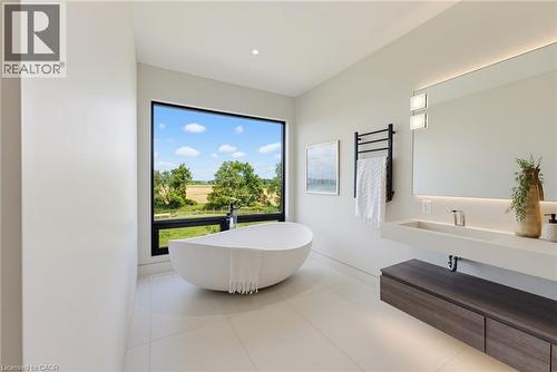 Freestanding soaking tub, expansive window with exterior scenery, floating vanity with integrated sink, large illuminated mirror, and wood-finish cabinetry - 5709 Forth Line, Hillsburg, ON 