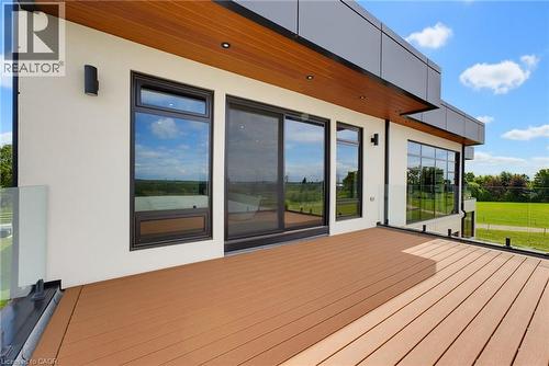 Spacious outdoor deck with wood-finish decking, glass panel railings, and modern black-framed windows - 5709 Forth Line, Hillsburg, ON 