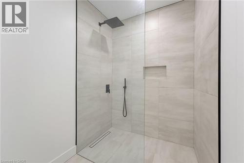 Walk-in shower with a glass enclosure, light-toned tilework, a built-in shower niche, a linear drain, and matte black fixtures - 5709 Forth Line, Hillsburg, ON 