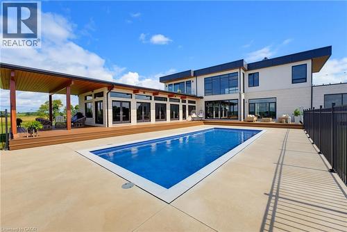 Modern residence featuring an expansive entertainer's backyard with resort-style saltwater swimming pool, surrounding concrete decking, covered lounge pavilion with wood-finish ceiling, and floor-to-c - 5709 Forth Line, Hillsburg, ON 