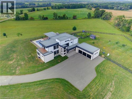Contemporary architectural design with a flat roofline, an integrated swimming pool, an expansive driveway, a detached multi-bay garage, and surrounding green space - 5709 Forth Line, Hillsburg, ON 