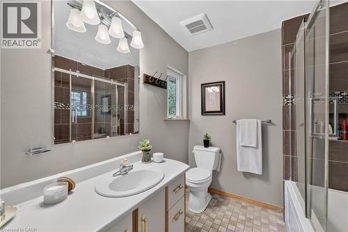 4 pc Bathroom featuring a vanity with a white countertop and integrated sink, a large wall-mounted mirror, a shower with sliding glass doors and brown tile surround, a toilet, and patterned tile floor - 2023 Latimer Crescent, Greater Sudbury, ON 