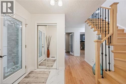 Entryway featuring a decorative glass door, mirrored closet doors, and a wood staircase with black wrought iron balusters - 345 Beechlawn Drive, Waterloo, ON 
