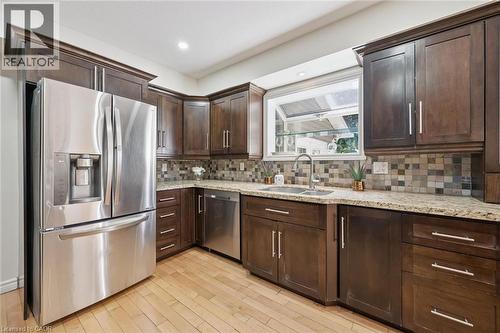 Kitchen featuring dark wood cabinetry, light-toned countertops, stainless steel appliances, a mosaic tile backsplash, and wood-finish flooring - 345 Beechlawn Drive, Waterloo, ON 