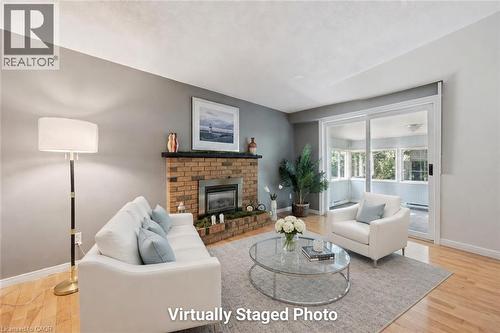 Bright living room showcasing a brick fireplace with integrated hearth, hardwood flooring, and expansive glass sliding doors opening to natural light - 345 Beechlawn Drive, Waterloo, ON 