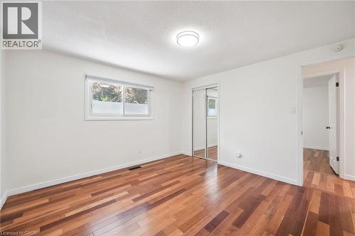 Bedroom featuring wood-finish flooring, a window with a roller blind, and mirrored closet doors - 345 Beechlawn Drive, Waterloo, ON 