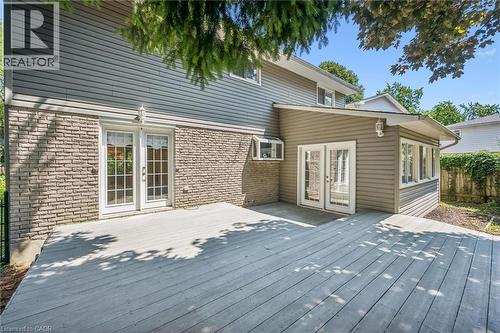 Expansive exterior deck offering multiple access points, featuring dual sets of white paneled French doors, grey horizontal siding, and a stone veneer foundation - 345 Beechlawn Drive, Waterloo, ON 