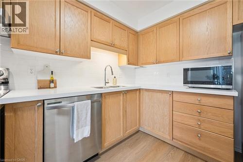 Wood-finish cabinetry, white subway tile backsplash, stainless steel dishwasher, and a stainless steel sink with a gooseneck faucet - 151 Clairfields Drive Unit# 3, Guelph, ON 