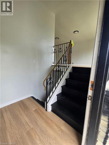 Wood-finish flooring with white baseboards, black-painted staircase, black wrought iron railing with wood handrail, and recessed ceiling lighting - 99 Cluthe Crescent, Kitchener, ON 