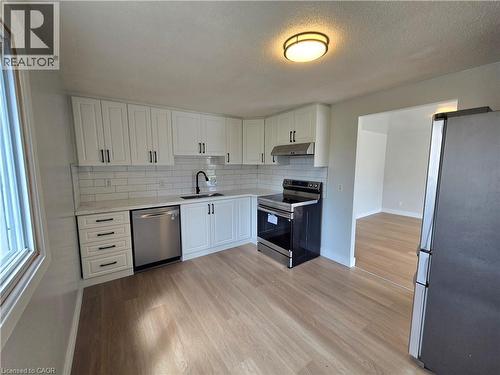 Kitchen featuring white shaker-style cabinetry, stainless steel appliances, a white subway tile backsplash, light-toned wood-finish flooring, and a contemporary flush-mount ceiling light - 99 Cluthe Crescent, Kitchener, ON 