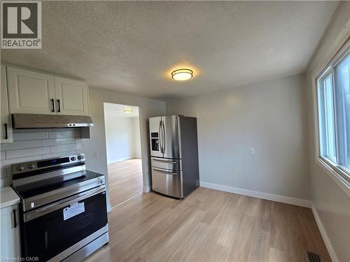 Kitchen featuring wood-finish flooring, white cabinetry with black hardware, stainless steel appliances, and a window - 99 Cluthe Crescent, Kitchener, ON 