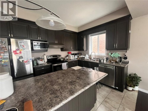 Kitchen featuring dark wood-finish cabinetry, stainless steel appliances, a center island with a speckled countertop, and tiled flooring - 298 Buttonbush Street, Waterloo, ON 
