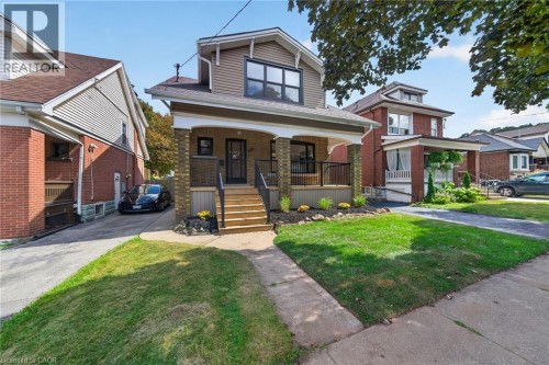 Craftsman-style exterior with siding and brick accents, covered front porch with dark railings, paved driveway, and a landscaped front yard with a walkway - 229 Park Row S, Hamilton, ON 